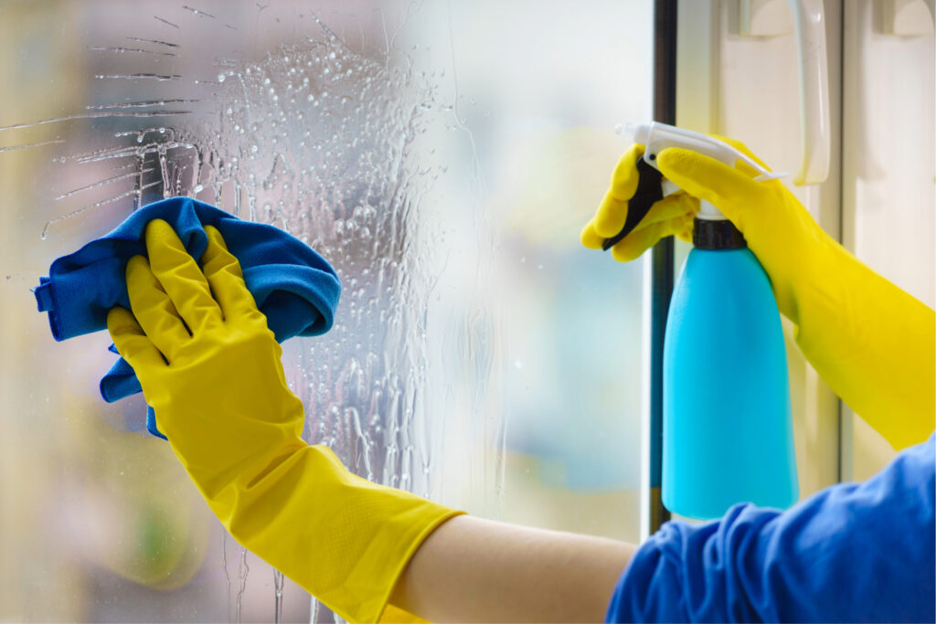Person sprutar fönsterputsmedel på glasruta med sprayflaska.